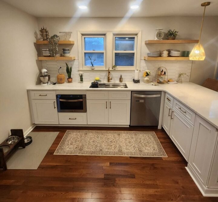 Modern kitchen with white cabinets, hardwood flooring, open shelving, and a central window offering natural light, located in a remodeled home in Dayton.